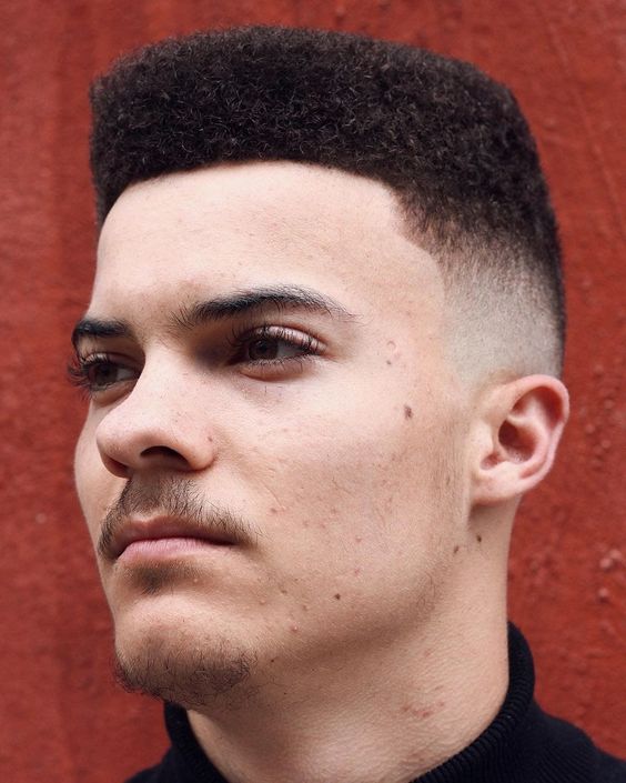 Curly flat top hairstyle for men, with a high, flat top of defined curls and faded sides.